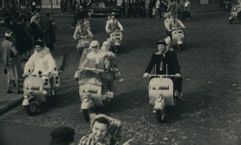 Movie still from “Ulysse” (1983), directed by Agnès Varda – A group of people on motor scooters driving down a street; Wide shot, High angle