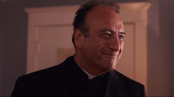 Movie still from “Unbroken: Path to Redemption” (2018), directed by Harold Cronk – A man wearing a priest's outfit smiling for the camera; Close Up shot, Low angle