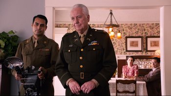 Movie still from “Unbroken: Path to Redemption” (2018), directed by Harold Cronk – An older man in a military uniform standing in front of two other men; Medium shot, Over the shoulder angle