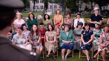 Movie still from “Unbroken: Path to Redemption” (2018), directed by Harold Cronk – A group of women sitting on chairs in front of a building; Wide shot, High angle
