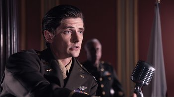 Movie still from “Unbroken: Path to Redemption” (2018), directed by Harold Cronk – A man in a military uniform is holding a microphone; Medium shot, Low angle