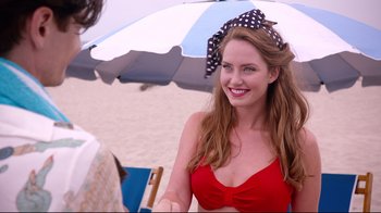 Movie still from “Unbroken: Path to Redemption” (2018), directed by Harold Cronk – A beautiful young lady in a red bikini under an umbrella on the beach; Close Up shot, Over the shoulder angle