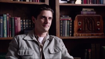 Movie still from “Unbroken: Path to Redemption” (2018), directed by Harold Cronk – A man sitting in front of a book shelf; Medium shot, Over the shoulder angle