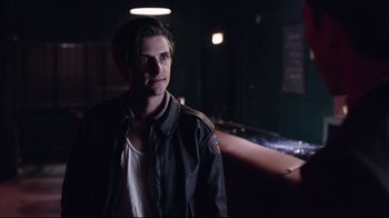 Movie still from “Unbroken: Path to Redemption” (2018), directed by Harold Cronk – A man in a leather jacket standing in a dark room; Close Up shot, Over the shoulder angle