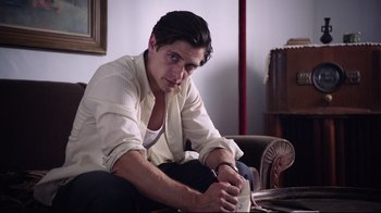 Movie still from “Unbroken: Path to Redemption” (2018), directed by Harold Cronk – A man sitting on a couch writing on a piece of paper; Medium shot, Low angle