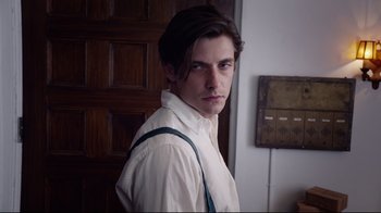 Movie still from “Unbroken: Path to Redemption” (2018), directed by Harold Cronk – A man with long hair wearing a white shirt and suspenders standing in front of a wooden door; Close Up shot, Low angle