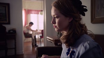 Movie still from “Unbroken: Path to Redemption” (2018), directed by Harold Cronk – A woman sitting in a living room with a man sitting in the background; Medium shot, Over the shoulder angle