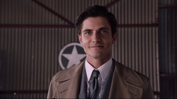 Movie still from “Unbroken: Path to Redemption” (2018), directed by Harold Cronk – A man wearing a suit and tie in front of a wall; Close Up shot, Over the shoulder angle