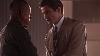 Movie still from “Unbroken: Path to Redemption” (2018), directed by Harold Cronk – A man wearing a suit and tie talking to another man; Medium shot, Over the shoulder angle
