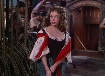 Movie still from “Unconquered” (1947), directed by Cecil B. DeMille – A woman in a red and black dress standing in front of ropes; Medium shot, Over the shoulder angle