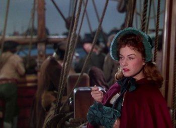 Movie still from “Unconquered” (1947), directed by Cecil B. DeMille – A woman in a red dress and green hat smoking a cigarette on a boat; Medium shot, Over the shoulder angle