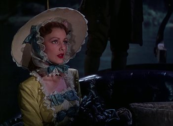 Movie still from “Unconquered” (1947), directed by Cecil B. DeMille – A woman wearing a hat sitting on top of a couch; Medium shot, Low angle