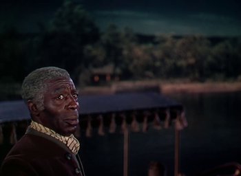 Movie still from “Unconquered” (1947), directed by Cecil B. DeMille – An older man standing next to a body of water at night; Medium shot, Over the shoulder angle