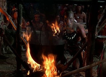 Movie still from “Unconquered” (1947), directed by Cecil B. DeMille – A man cooking food over a fire in an outdoor setting; Medium shot, High angle