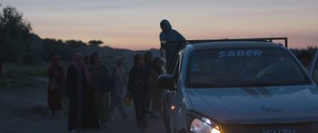 Movie still from “Under the Fig Trees” (2021), directed by Erige Sehiri – A group of people walking on the side of the road; Wide shot, Low angle