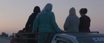 Movie still from “Under the Fig Trees” (2021), directed by Erige Sehiri – A group of people sitting on top of a car; Medium shot, Low angle