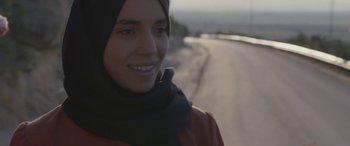 Movie still from “Under the Fig Trees” (2021), directed by Erige Sehiri – A young woman wearing a headscarf standing next to a road; Close Up shot, Low angle