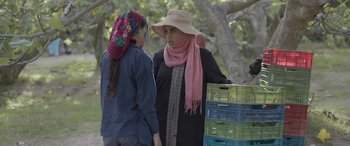 Movie still from “Under the Fig Trees” (2021), directed by Erige Sehiri – A woman wearing a hat and scarf talking to another woman; Medium shot, Over the shoulder angle