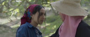 Movie still from “Under the Fig Trees” (2021), directed by Erige Sehiri – A woman wearing a hat and a scarf talking to another woman; Close Up shot, Over the shoulder angle
