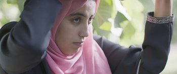 Movie still from “Under the Fig Trees” (2021), directed by Erige Sehiri – A young woman wearing a pink headscarf looking down; Close Up shot, Over the shoulder angle