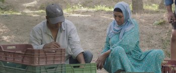 Movie still from “Under the Fig Trees” (2021), directed by Erige Sehiri – A man and a woman sitting next to each other on the ground; Medium shot, High angle