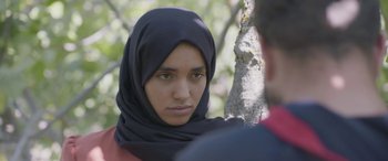 Movie still from “Under the Fig Trees” (2021), directed by Erige Sehiri – A woman wearing a black headscarf is standing next to a man; Close Up shot, Over the shoulder angle