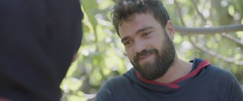 Movie still from “Under the Fig Trees” (2021), directed by Erige Sehiri – A man with a goatee is smiling for the camera; Close Up shot, Over the shoulder angle