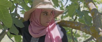 Movie still from “Under the Fig Trees” (2021), directed by Erige Sehiri – A woman wearing a hat and a pink scarf; Close Up shot, Low angle