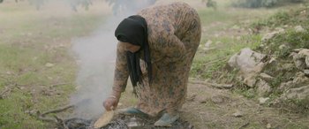 Movie still from “Under the Fig Trees” (2021), directed by Erige Sehiri – An old woman is cooking a meal on the ground; Wide shot, High angle