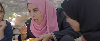 Movie still from “Under the Fig Trees” (2021), directed by Erige Sehiri – A woman in a pink headscarf is eating a sandwich; Close Up shot, Over the shoulder angle
