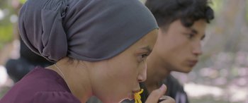 Movie still from “Under the Fig Trees” (2021), directed by Erige Sehiri – A woman in a headscarf is eating a piece of food; Close Up shot, Over the shoulder angle