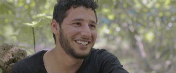 Movie still from “Under the Fig Trees” (2021), directed by Erige Sehiri – A person smiling with trees in the background; Close Up shot, Low angle