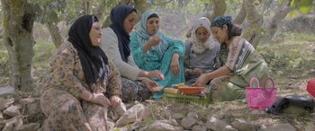Movie still from “Under the Fig Trees” (2021), directed by Erige Sehiri – A group of women sitting on the ground eating food; Wide shot, High angle