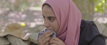 Movie still from “Under the Fig Trees” (2021), directed by Erige Sehiri – A young girl wearing a pink headscarf is holding her mouth open; Close Up shot, Over the shoulder angle
