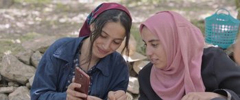Movie still from “Under the Fig Trees” (2021), directed by Erige Sehiri – Two young women are looking at a cell phone; Medium shot, Low angle