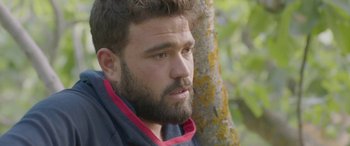 Movie still from “Under the Fig Trees” (2021), directed by Erige Sehiri – A man with a goatee is leaning against a tree; Close Up shot, Over the shoulder angle