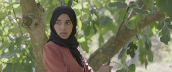 Movie still from “Under the Fig Trees” (2021), directed by Erige Sehiri – A woman in a black headscarf is holding a stick; Close Up shot, Low angle
