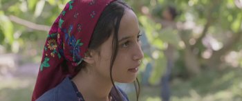 Movie still from “Under the Fig Trees” (2021), directed by Erige Sehiri – A young girl with a red headscarf looking to her left; Close Up shot, Over the shoulder angle