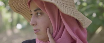 Movie still from “Under the Fig Trees” (2021), directed by Erige Sehiri – A young woman wearing a pink head covering; Close Up shot, Low angle
