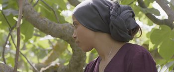 Movie still from “Under the Fig Trees” (2021), directed by Erige Sehiri – A woman wearing a headscarf is standing next to a tree; Close Up shot, Over the shoulder angle