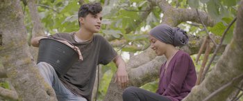 Movie still from “Under the Fig Trees” (2021), directed by Erige Sehiri – A man and a woman sitting next to a tree; Medium shot, Over the shoulder angle