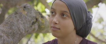 Movie still from “Under the Fig Trees” (2021), directed by Erige Sehiri – A young woman wearing a headscarf looking to her left; Close Up shot, Over the shoulder angle