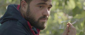 Movie still from “Under the Fig Trees” (2021), directed by Erige Sehiri – A person with a beard smoking; Close Up shot, Low angle