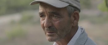 Movie still from “Under the Fig Trees” (2021), directed by Erige Sehiri – An older man wearing a hat looking at the camera; Close Up shot, Over the shoulder angle