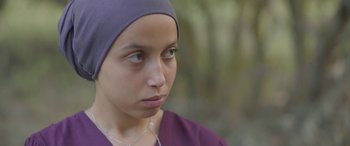 Movie still from “Under the Fig Trees” (2021), directed by Erige Sehiri – A woman wearing a purple shirt and a purple headscarf; Close Up shot, Over the shoulder angle