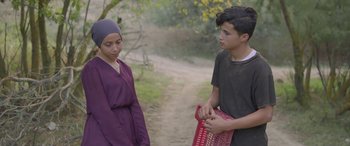 Movie still from “Under the Fig Trees” (2021), directed by Erige Sehiri – A young man and a young woman standing next to each other on a dirt path; Medium shot, Over the shoulder angle