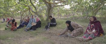 Movie still from “Under the Fig Trees” (2021), directed by Erige Sehiri – A group of people sitting on the ground under a tree; Wide shot, High angle
