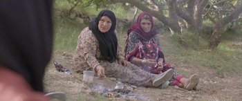 Movie still from “Under the Fig Trees” (2021), directed by Erige Sehiri – A couple of women sitting next to each other on the ground; Wide shot, High angle