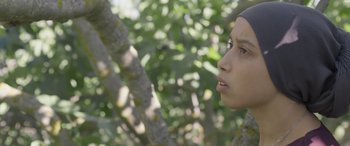 Movie still from “Under the Fig Trees” (2021), directed by Erige Sehiri – A young woman is standing next to a tree; Close Up shot, Over the shoulder angle