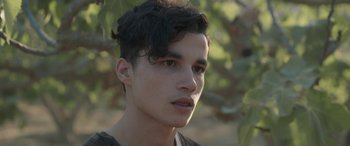 Movie still from “Under the Fig Trees” (2021), directed by Erige Sehiri – A young man is looking into the camera; Close Up shot, Over the shoulder angle